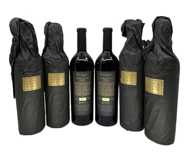 Five bottles of wine wrapped in black cloth with gold labels on a white surface.